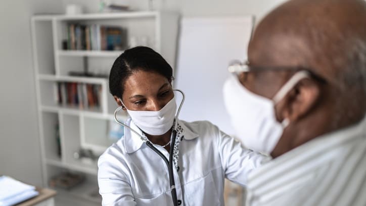 An elderly man wearing a face mask is being examined by a doctor.