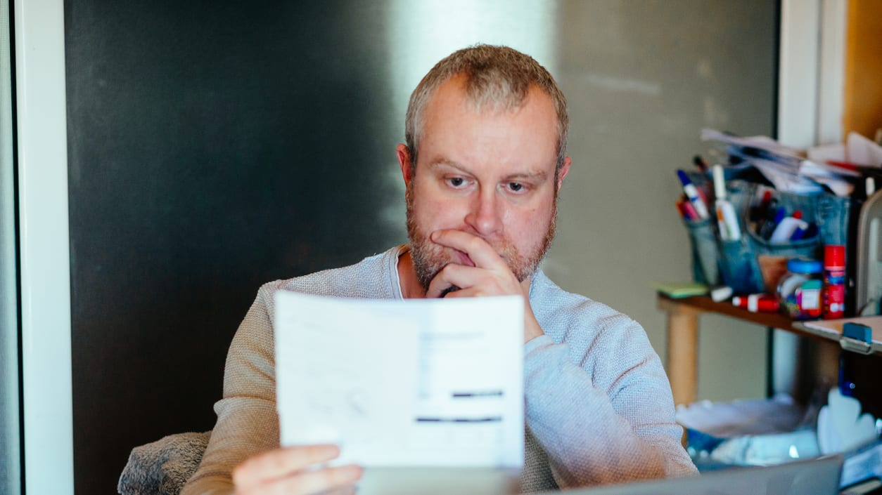 A man looking at a piece of paper in front of a laptop.