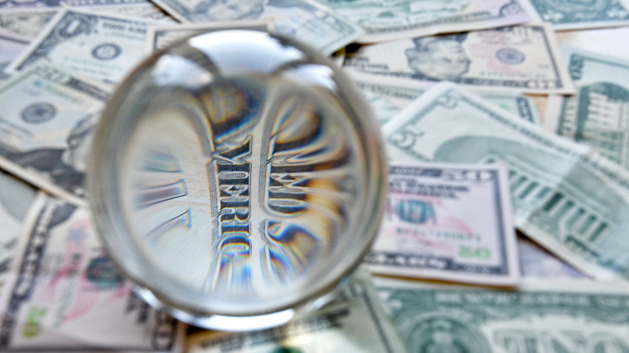 A glass ball sits on top of a pile of money.