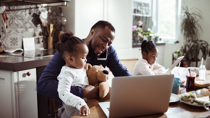 An man and his children using a laptop at the kitchen table.