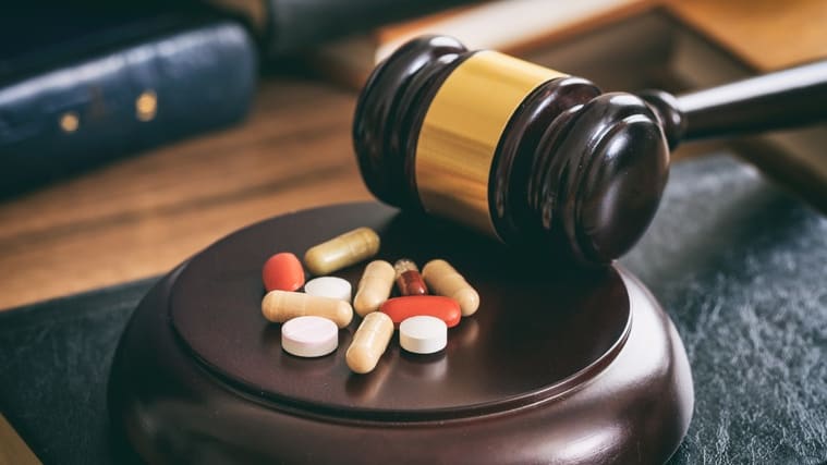 A judge's gavel and pills on top of a book.