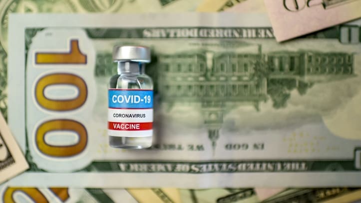 A bottle of coronavirus vaccine sits on top of a pile of money.