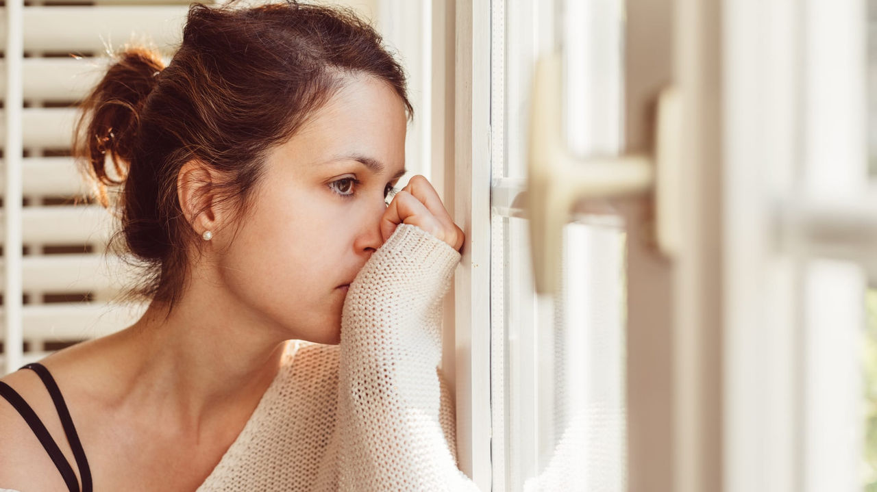 A woman looking out a window with her hand on her face.