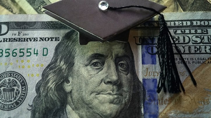 A graduation cap sits on top of a dollar bill.