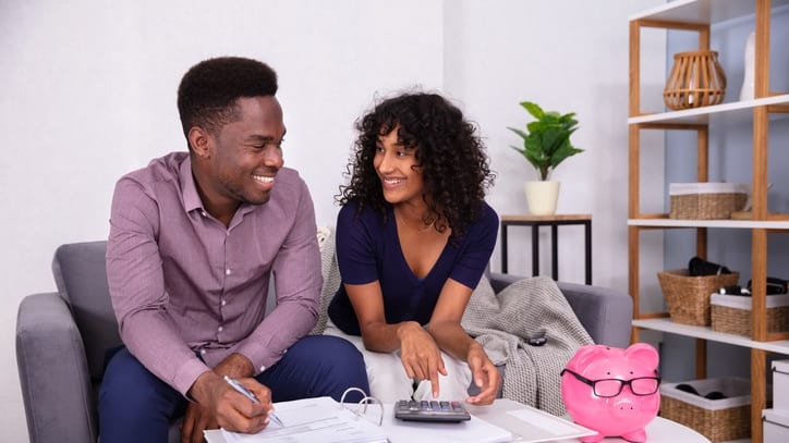 A man and woman sitting on a couch looking at a piggy bank.