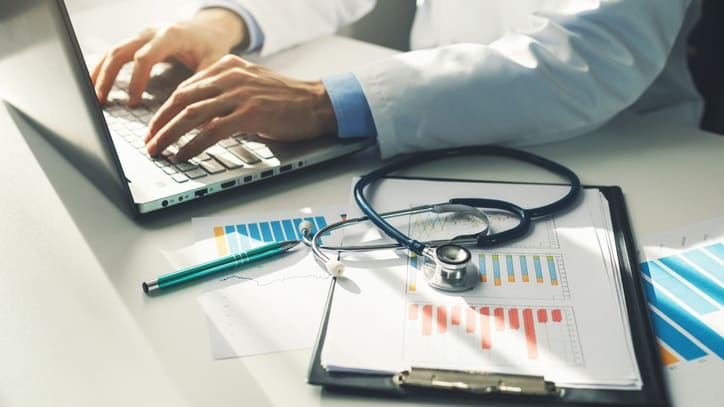 A doctor working on a laptop with a stethoscope.