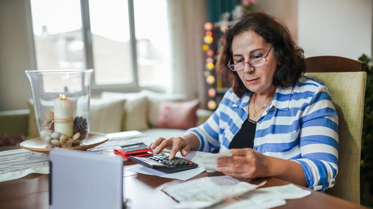 A woman is sitting at a table and using a calculator.