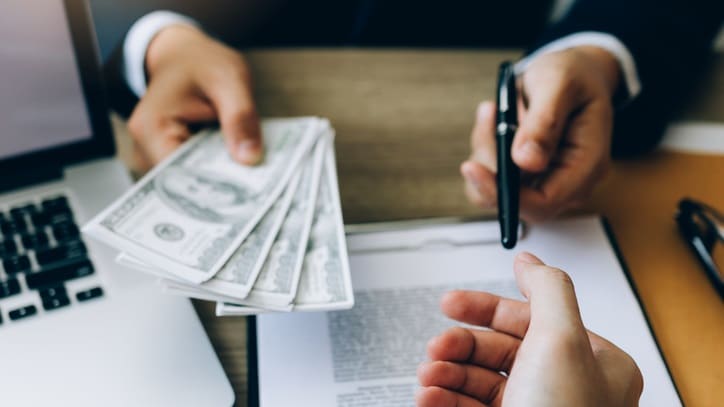 A person handing money to another person at a desk.