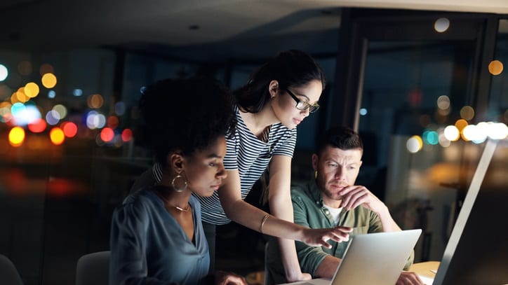 A group of people looking at a laptop at night.