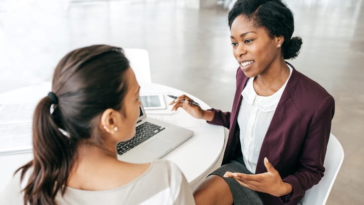 Two women talking in an office with a laptop.