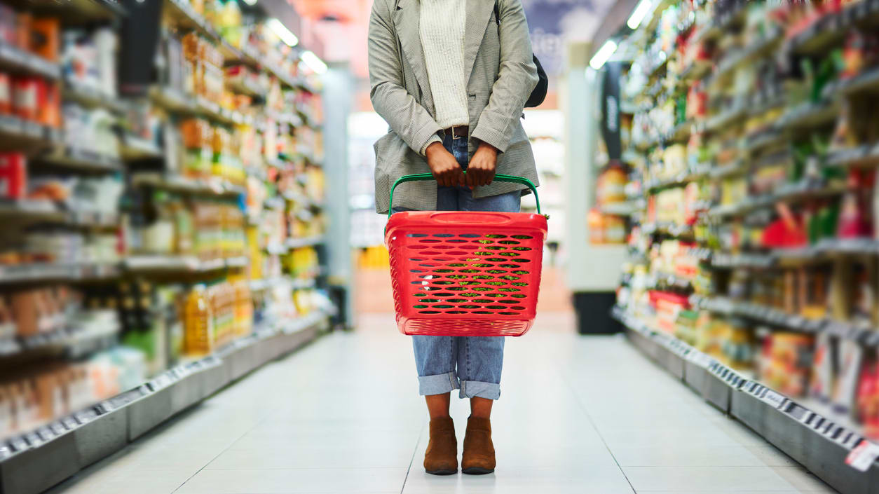 A woman holding a shopping basket in a grocery store.