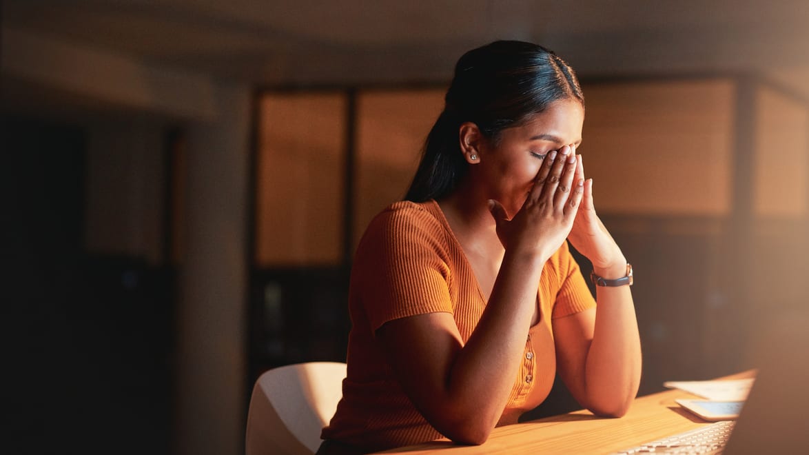 A woman is covering her face while sitting at a desk.