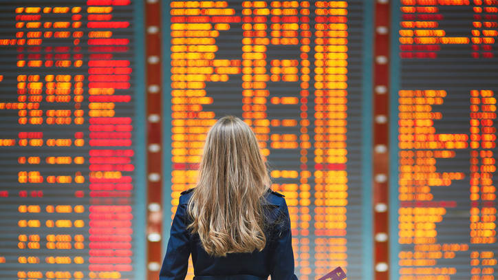 A woman is standing in front of an airport departure board.