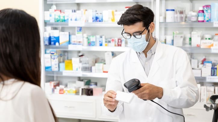 A man wearing a mask is standing in front of a pharmacy.