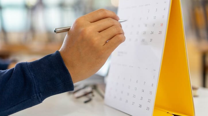 A person writing on a calendar with a pen.