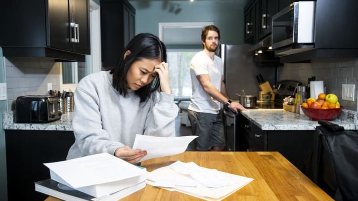 A man and woman in a kitchen with papers in front of them.
