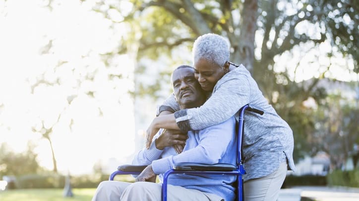 An elderly couple hugging in a wheelchair.