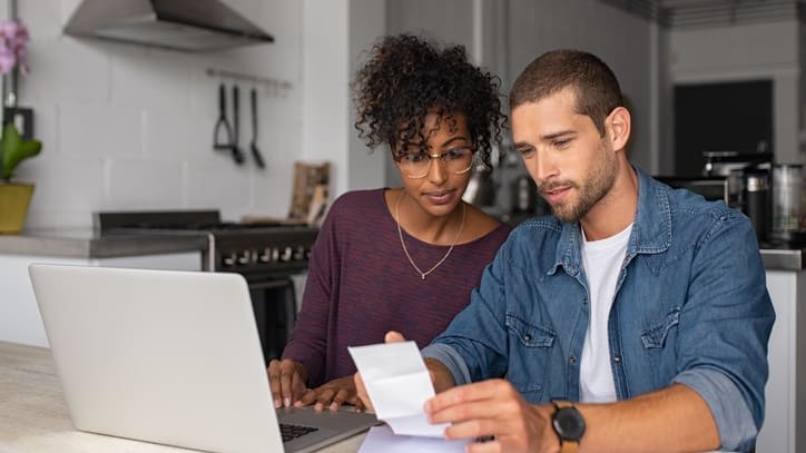 A man and woman are looking at their bills on a laptop.