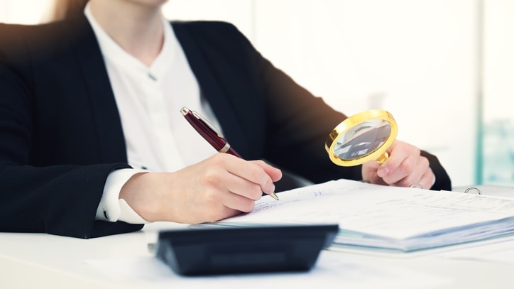A business woman is looking at a document with a magnifying glass.
