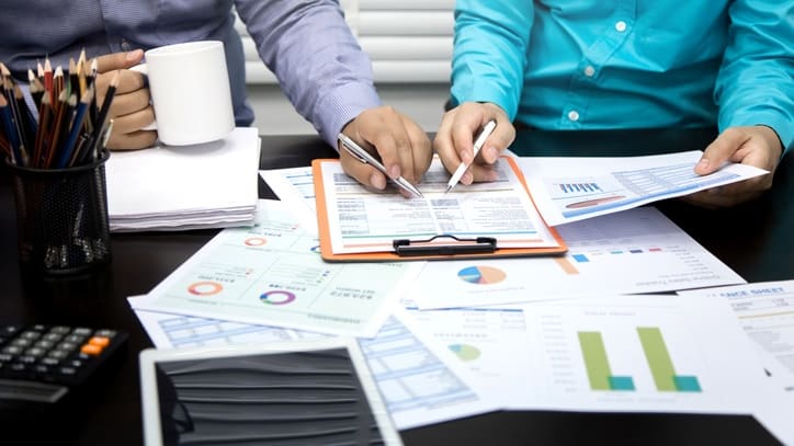 Two people in business clothes working on paperwork at a desk.