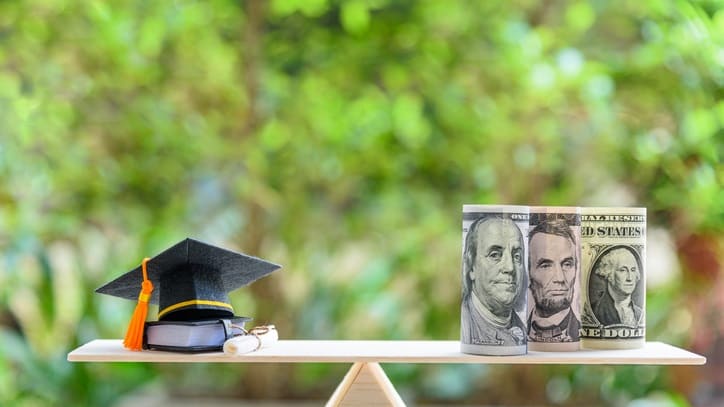 A graduation cap and money on a balance scale.