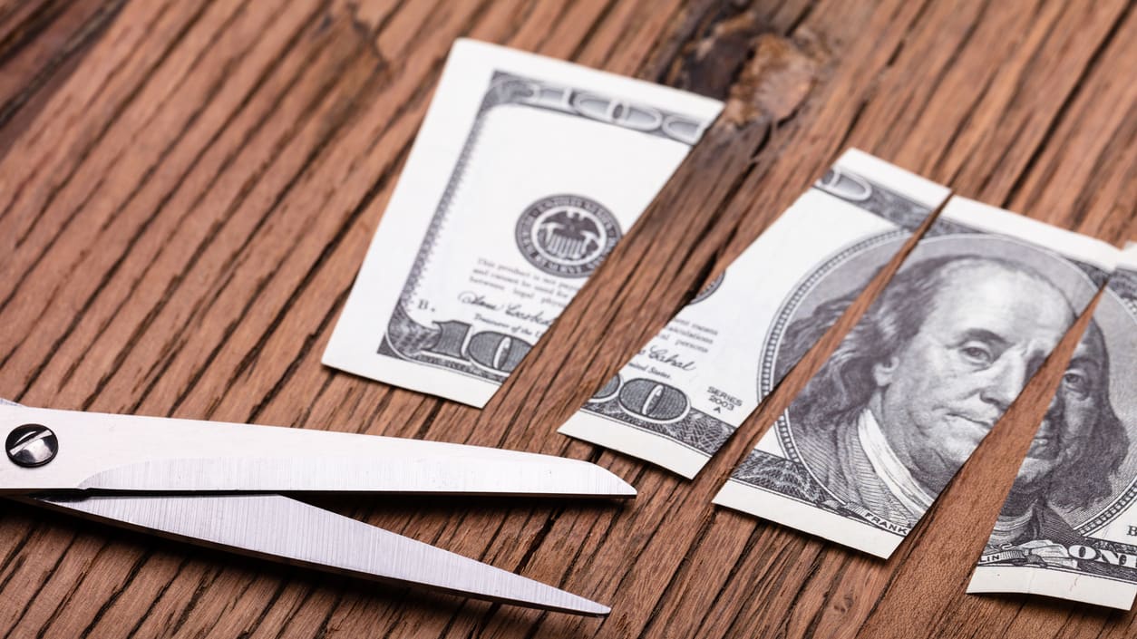 A pair of scissors on a wooden table with dollar bills.