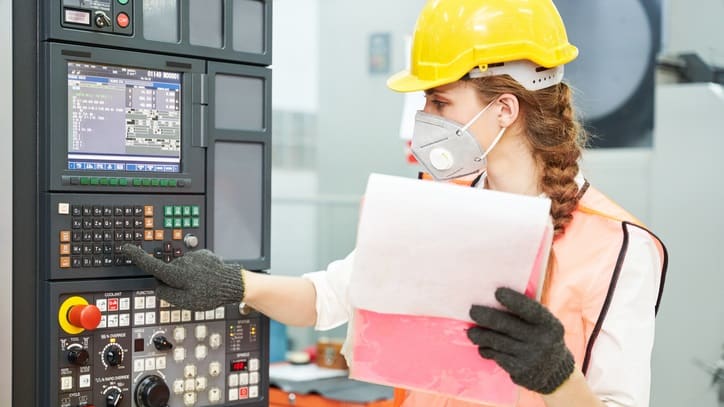 A woman in a hard hat is working on a cnc milling machine.