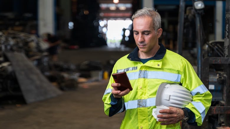 A man in a hard hat holding a cell phone in a factory.