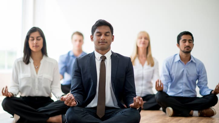 A group of business people meditating in a room.