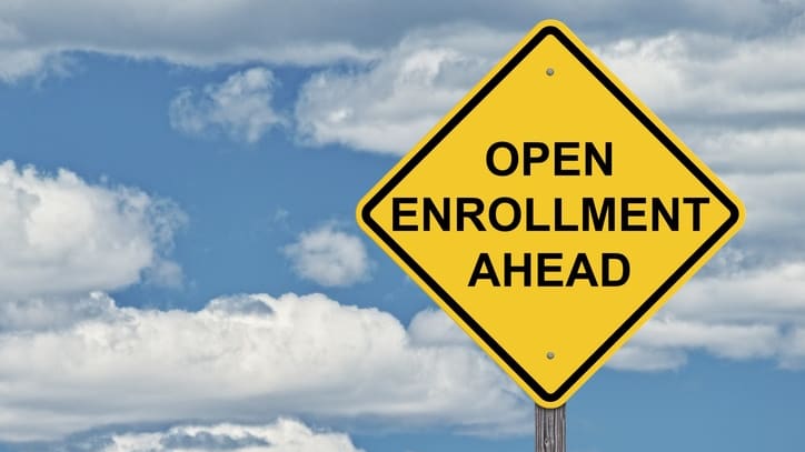 A yellow sign that says open enrollment ahead against a cloudy sky.