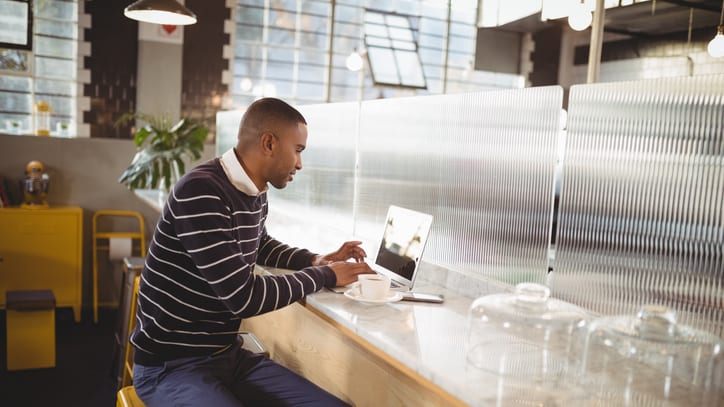 A man sitting on a stool in a coffee shop using a laptop.