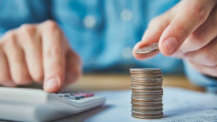 A person is holding a stack of coins and a calculator.