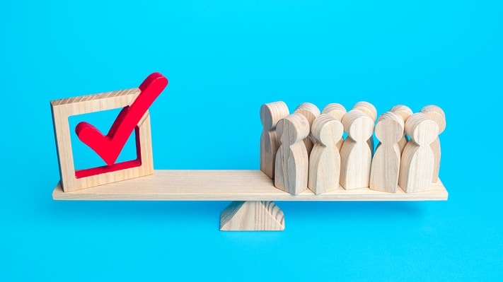 A wooden scale with people on it and a check mark on it.