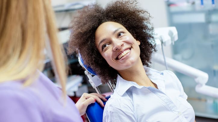 A woman smiles while sitting in a dentist's chair.