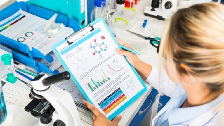 A woman in a lab coat is looking at a clipboard.