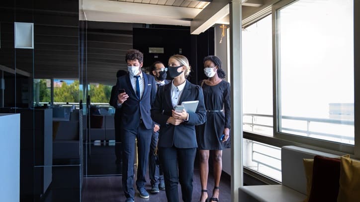 A group of business people wearing face masks walking in an office.