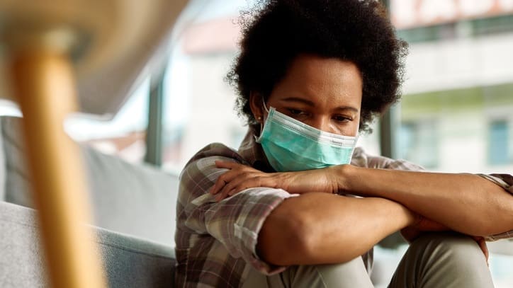 A woman wearing a surgical mask sitting on a couch.
