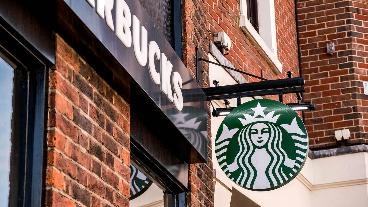A starbucks sign hangs from the side of a brick building.