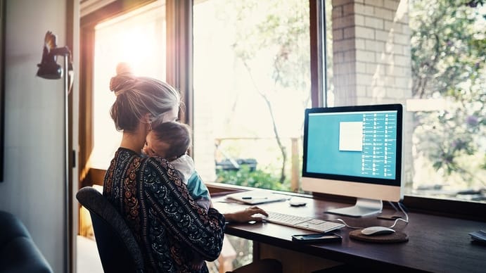 A woman working at her computer with a baby in her lap.