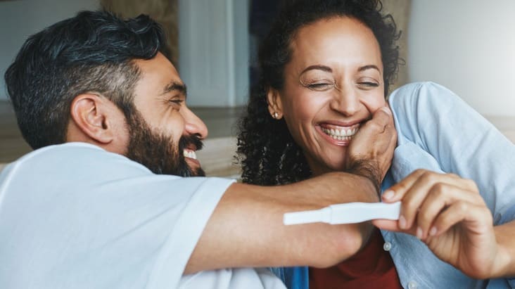 A man and woman smiling while holding a pregnancy test.