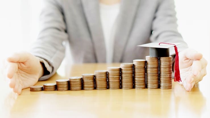 A woman holding a graduation cap on a stack of coins.