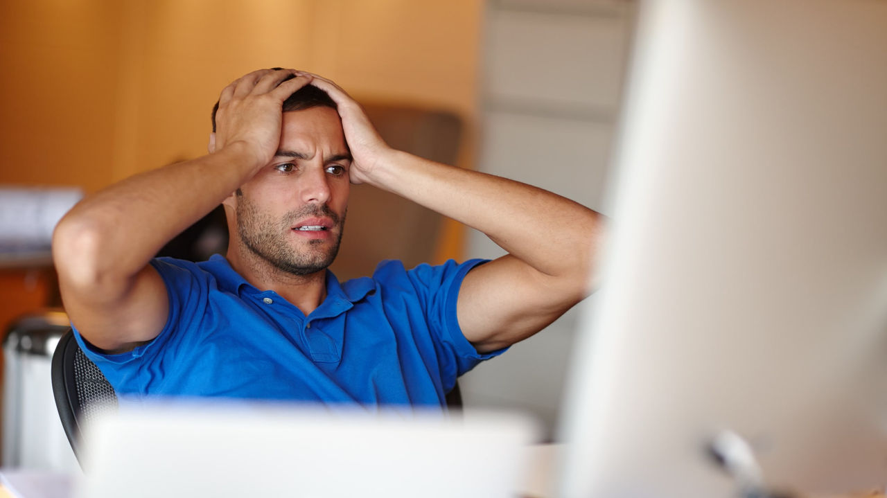 A man holding his head in front of a computer screen.