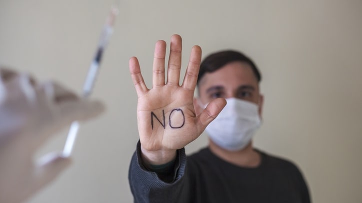 A man with a mask holding a syringe with the word no written on it.