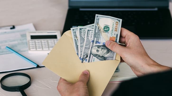 A hand holding a envelope with money in it.