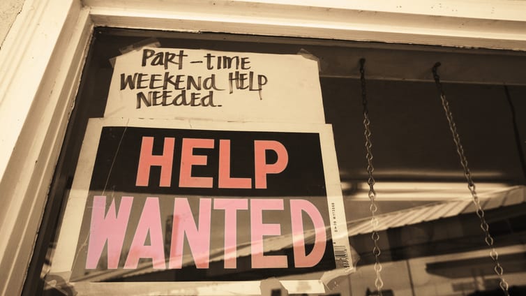 A sign that says help wanted hangs in a store window.