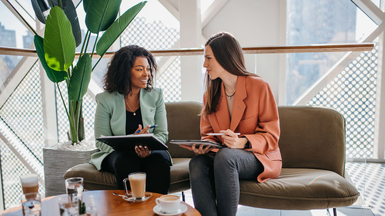 Two business women sitting on a couch in a conference room.