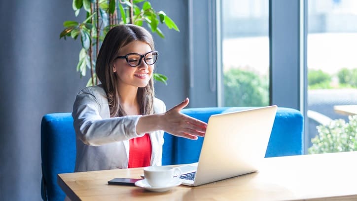 A woman in glasses is sitting at a table with a laptop.