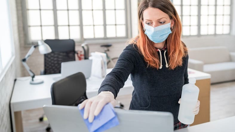 A woman wearing a face mask cleaning a laptop.