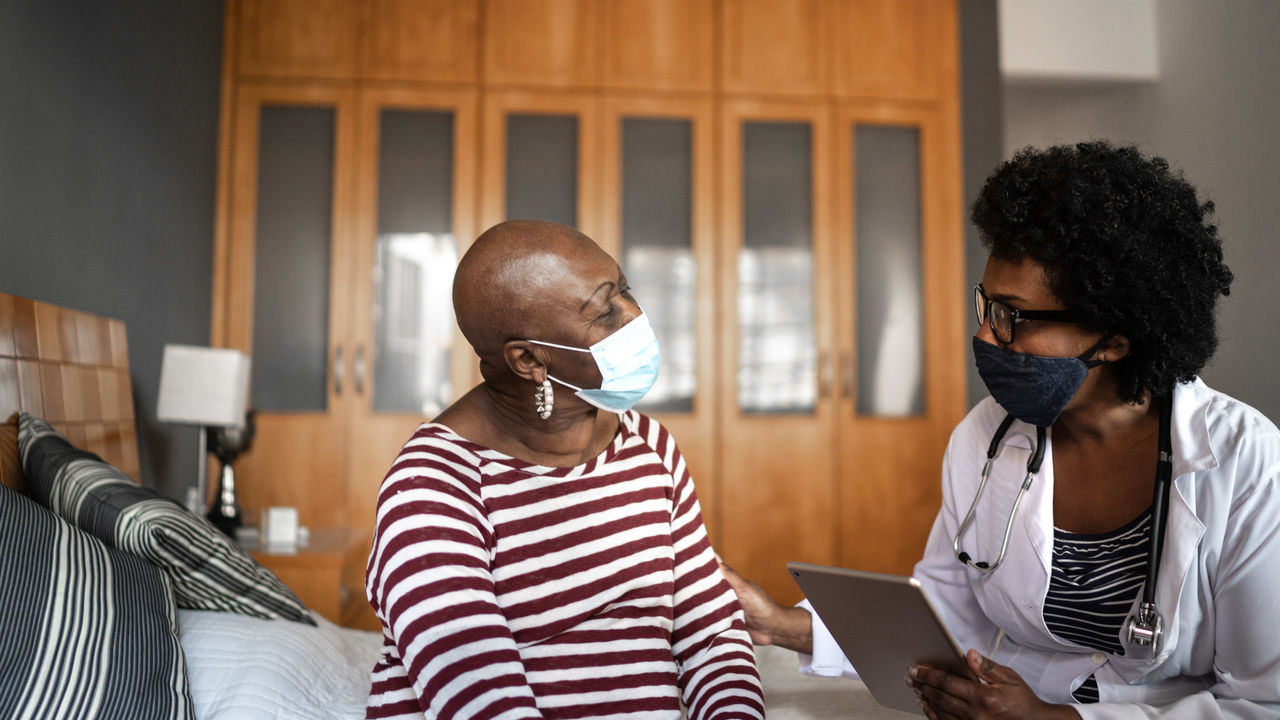 A woman wearing a face mask is talking to a doctor in a hospital bed.