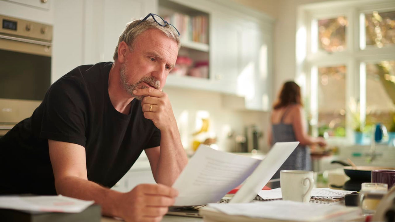 A man sitting at the kitchen counter looking at paperwork.